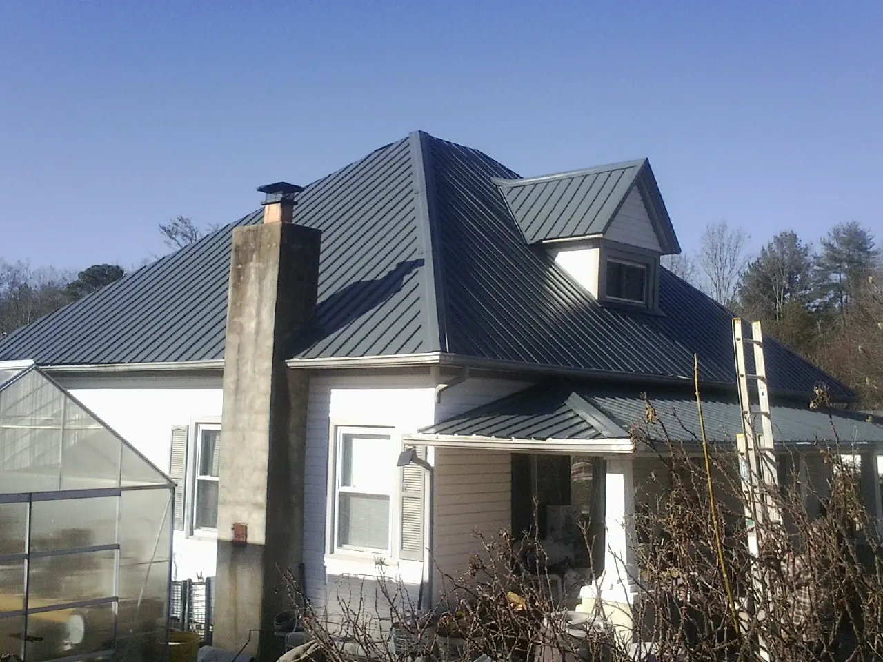 Dark blue standing seam metal roof on a white farmhouse with dormer — Slate & Tile Roof Repair by Roofing Brothers in Mc Callsburg