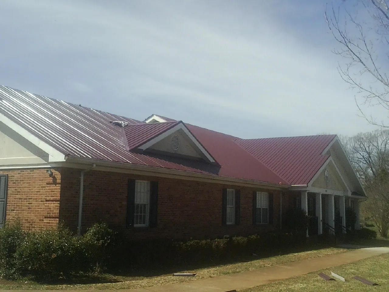 Red metal roof with gabled entries on a long brick building, from a Hail Damage Roof Repair job in Mc Callsburg