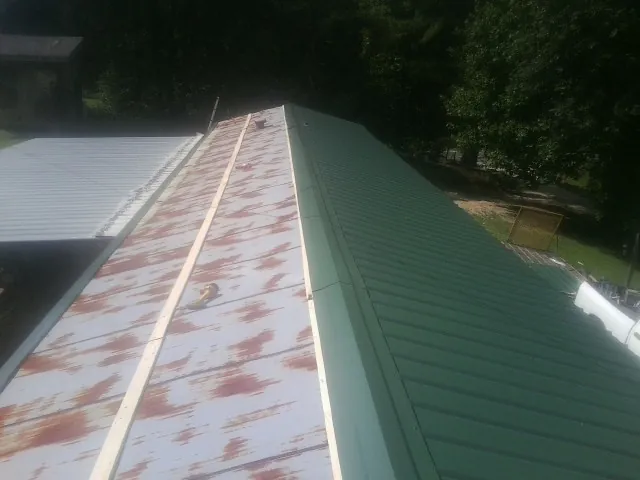 Old rusted panels beside newly installed green metal roofing — Wind Damage Roof Repair by Roofing Brothers in Mc Callsburg