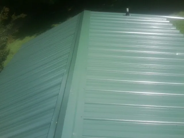 New green metal panels meeting at the ridge of a roof — Flat Roof Repair work by our crew in Mc Callsburg