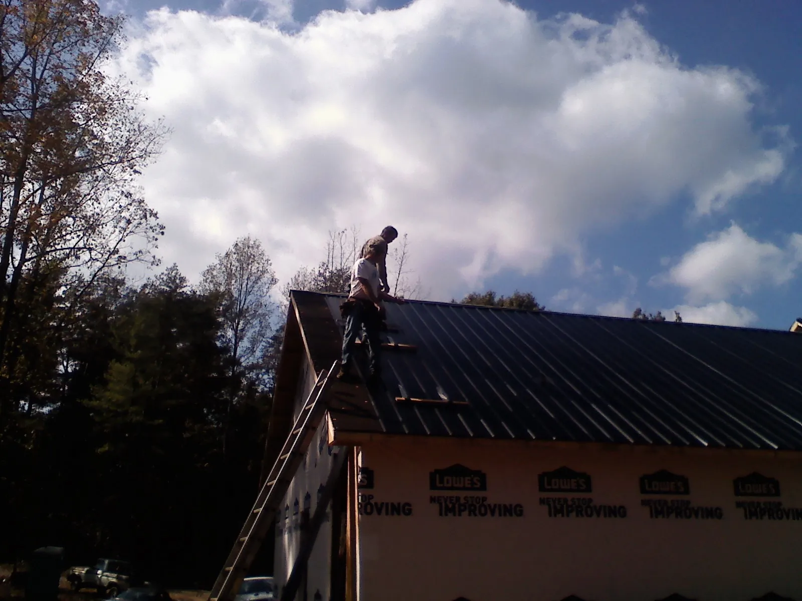 Roofer fastening dark metal panels high against a cloudy sky, from a Roof Inspection job in Mc Callsburg