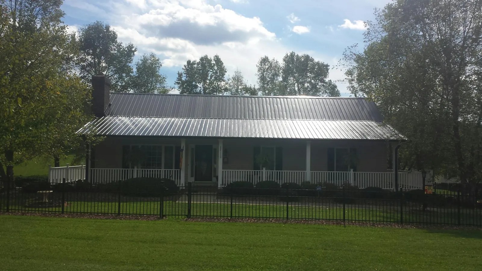 Gray metal roof on a brick ranch with a full width front porch — Gutter Guard Installation work by our crew in Mc Callsburg