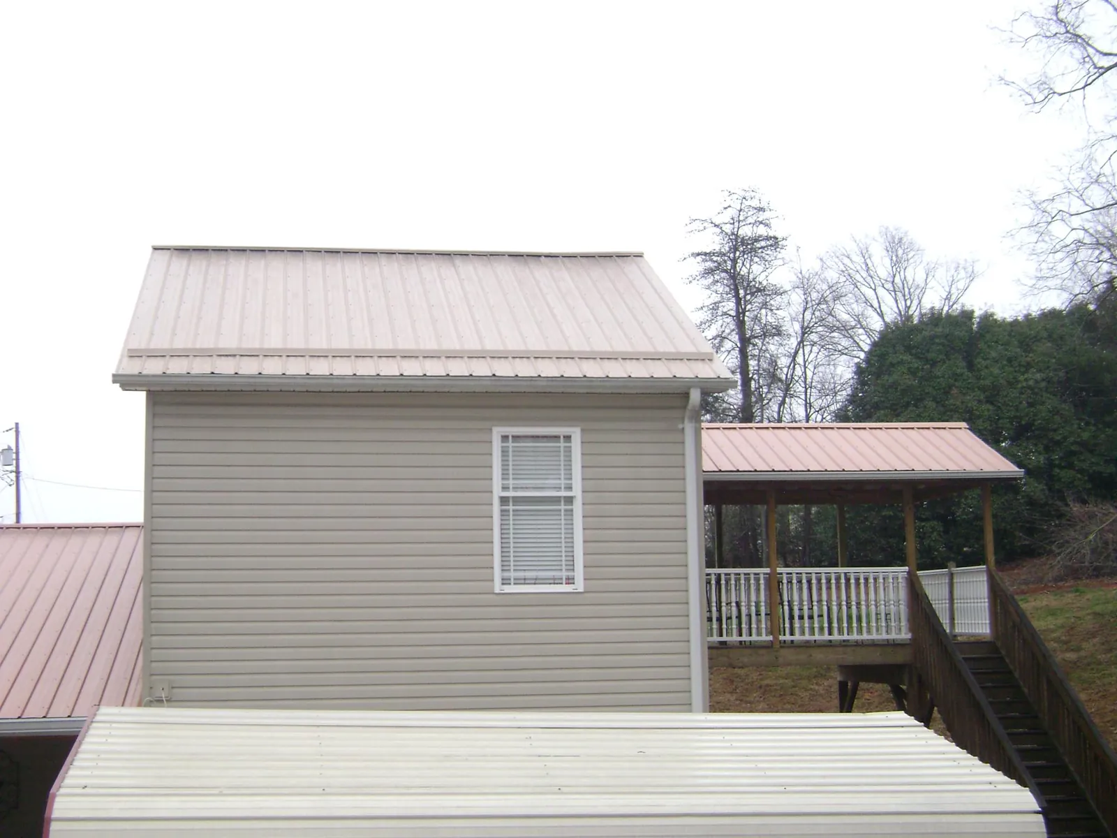 Tan metal roofs on a two story addition and attached porch, from a Roof Replacement job in Mc Callsburg
