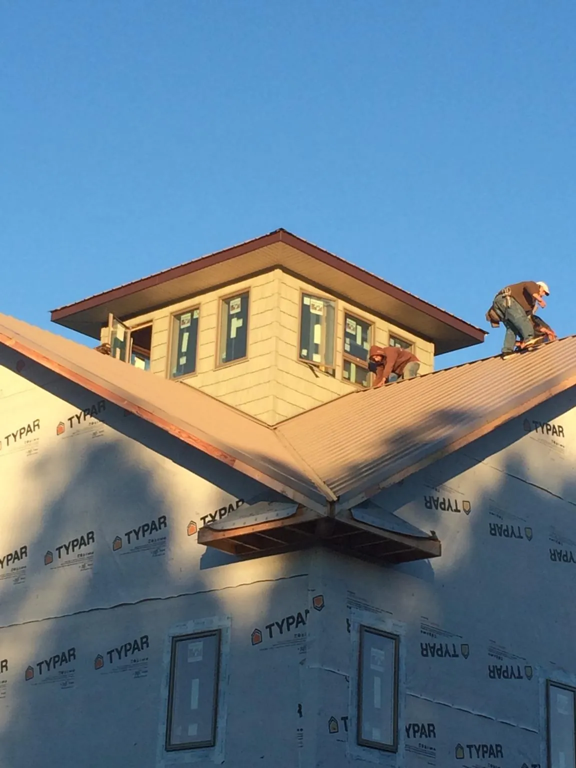 Roofers working around a rooftop cupola on a new metal roof at sunset — Roof Waterproofing in Mc Callsburg by Roofing Brothers